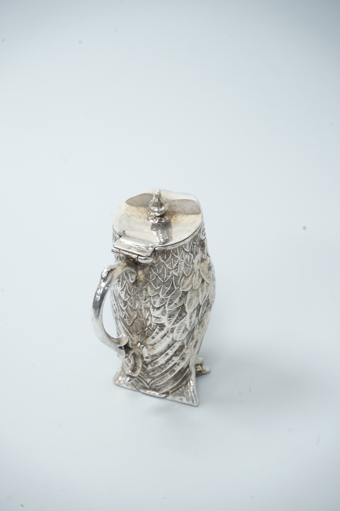A novelty white metal single handled mustard pot, modelled as a free-standing owl, with hinged cover and textured 'feathers', unmarked, height 95mm.
